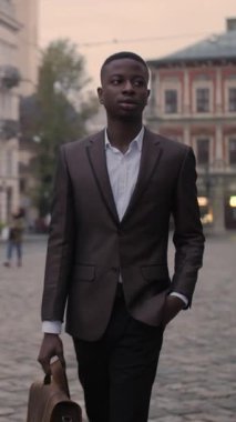 Kendine güvenen, şık takım elbiseli bir işadamı. Şehir caddesinde yürüyor ve kahverengi evrak çantası taşıyor. Bulanık arkaplan. İş ve başarı kavramı.