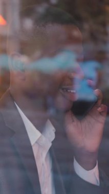 Serious afro american man in suit talking on mobile while sitting at cafe during a break. Young businessman having distance working conversation indoors.