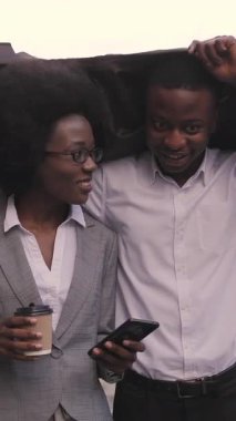 Şehir caddesinde yürürken ceketinin altında yağmurdan saklanan mutlu Afro-Amerikalı erkek ve kadın. İki iş ortağı iş toplantısına gidiyor..