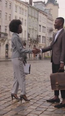 Genç Afro-Amerikan kadın ve sokakta tokalaşan yakışıklı adamın tam boy portresi. Dışarıda birbirini selamlayan iki iş ortağı..