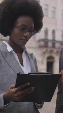 Başarılı iş adamı ve iş kadını şehir caddesinde birlikte konuşuyor ve panoya bakıyor. Resmi olarak iki meslektaş açık havada iş konularını tartışıyor..