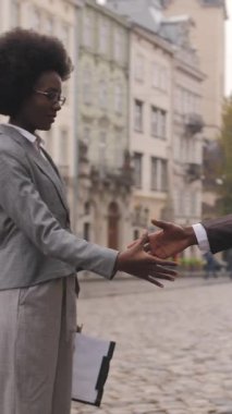 Resmi giyinmiş iki Afro-Amerikan ortak şehir caddesinde dururken el sıkışıyor. Deri evrak çantası tutan bir adam, elinde pano tutan bir kadın..