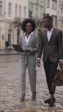 Dosyasıyla güzel bir kadın ve evrak çantalı yakışıklı bir adam sokakta yürüyor ve konuşuyor. Şık giyinmiş iki Afrikalı iş arkadaşı dışarıda poz veriyor..