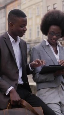 Mutlu Afro-Amerikan erkek ve kadın şık giyiniyor. Açık havuzda otururken çalışma saatlerini tartışıyorlar. Ortaklık kavramı.