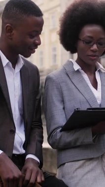 Mutlu Afro-Amerikan erkek ve kadın şık giyiniyor. Açık havuzda otururken çalışma saatlerini tartışıyorlar. Ortaklık kavramı.