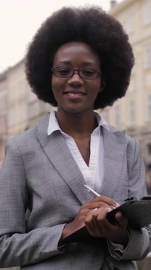 Afro-Afrikalı bir iş kadınının şehrin caddesinde elinde pano tutarken şık kıyafetler giymesi ön planda. Başarılı kariyer kavramı.