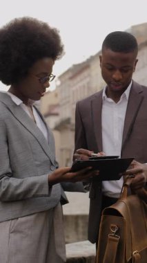 Portrait of two busy african people sign a contract on clipboard while standing on city street. Female assistant make a deal with male employer.
