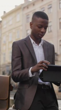 Takım elbiseli gülümseyen Afrikalı işadamı tablet ekranına bakıyor ve mutluluğu ifade etmek için yumruğunu sallıyor. İş yerinde haberler iyi. Başarılı bir kariyer..