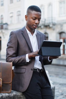Takım elbiseli genç profesyonel bir adam şehir ortamında dışarıda dururken tablet kullanıyor.