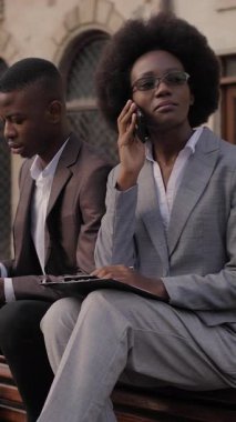 Erkek partner tahta bankta otururken ve dijital tablet kullanırken Afro-Amerikan kadın hareketli sohbetler yapıyor. Modern aletler ve uzaktan çalışma kavramı.