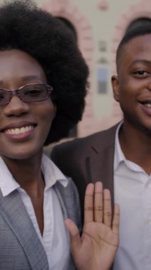 Gülümseyen Afrikalı bir adam ve takım elbiseli bir kadın şehrin caddesinde birlikte durup modern akıllı telefondan selfie çekiyorlar. Dışarıda mutlu ortaklar.