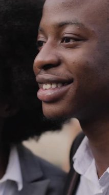 Gülümseyen Afrikalı bir adam ve takım elbiseli bir kadın şehrin caddesinde birlikte durup modern akıllı telefondan selfie çekiyorlar. Dışarıda mutlu ortaklar.