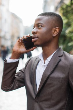 Takım elbiseli ve beyaz gömlekli genç bir adam şehir caddesinde yürürken telefonla konuşuyor.