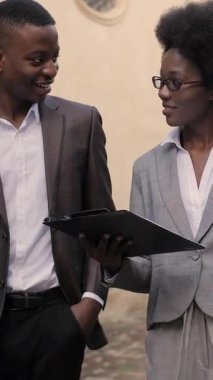 Dosyasıyla çekici bir kadın ve evrak çantalı yakışıklı bir adam sokakta dikilip iletişim kuruyor. Afro-Amerikalı iş arkadaşları açık havada bazı iş konularını tartışıyor..