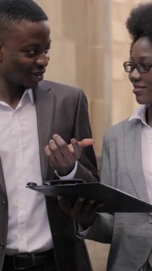 Dosyasıyla çekici bir kadın ve evrak çantalı yakışıklı bir adam sokakta dikilip iletişim kuruyor. Afro-Amerikalı iş arkadaşları açık havada bazı iş konularını tartışıyor..