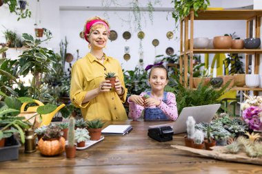 Bir kadın ve bir kız güzel bir çiçekçide çiçek tutarken gülümsüyorlar.