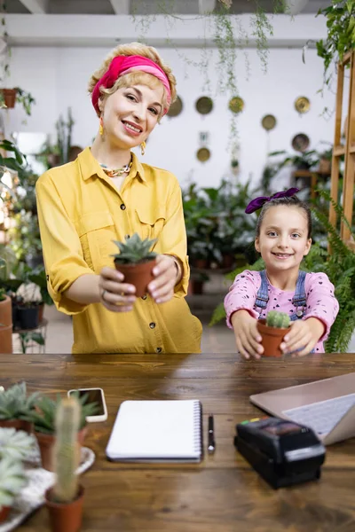 Bir kadın ve genç bir kız, küçük saksıları tutarken gülümsüyorlar.