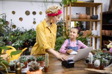 Bir kadın ve bir kız yeşillik ve bitkilerle çevrili bir fabrikada birlikte çalışıyorlar.