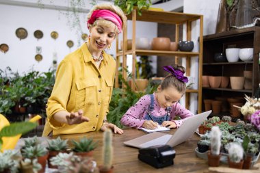 Bir kadın ve genç bir kız yeşillik ve sularla çevrili bir fabrikada birlikte çalışıyorlar.