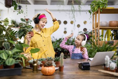 Bir kadın ve bir kız bitkilerle dans ediyorlar. Parlak, sera gibi bir yerde.