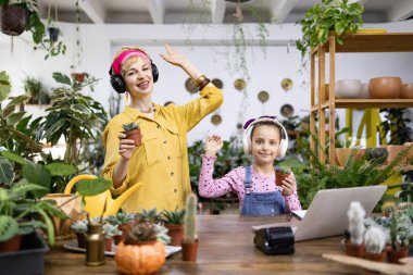 Bir kadın ve bir kız çiçekçide birlikte vakit geçiriyorlar, her biri küçük bir saksı suyu tutuyor.