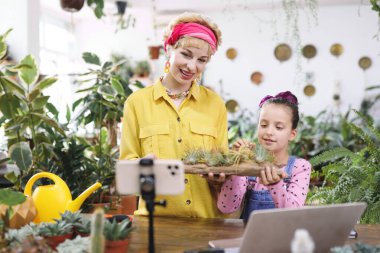 Bir kadın ve genç bir kız muhtemelen bir video için ahşap bir saksıda hava bitkileri tutuyorlar.