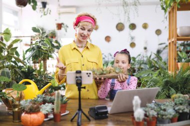Bir kadın ve genç bir kız muhtemelen bir video için ahşap bir saksıda hava bitkileri tutuyorlar.