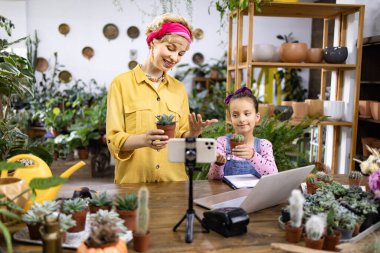 Bir anne ve kızı bir bitki dükkanında sulandırıcılarla ilgili bir video çekiyor.