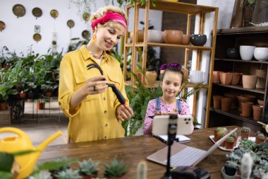 Bir kadın ve bir kız, sosyal medya için içerik yaratan bir bitki dükkanında birlikte bir bahçe bloğu çekiyorlar.