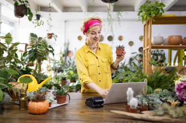 Sarı gömlekli bir kadın, bir fabrikada dizüstü bilgisayarla çalışırken sulu bir şey tutuyor.
