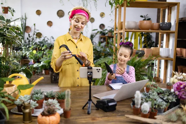 Bir kadın ve kızı internetteki seyircileri için alet ve dizüstü bilgisayar kullanarak bahçıvanlık dersi veriyorlar.