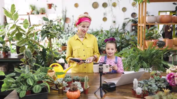 A woman and her daughter are teaching a gardening lesson using tools and a laptop for their online audience A woman and her daughter are teaching a gardening lesson using tools and a laptop for their online audience