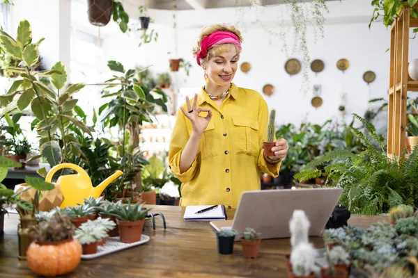 Sarı tişörtlü bir kadın, bir fabrikadaki video görüşmesinde el kol hareketi yaparken küçük bir kaktüs tutuyor.