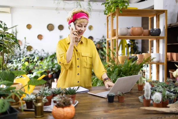 Sarı tişörtlü bir kadın, bir fabrikada dizüstü bilgisayarla konuşurken telefonla konuşuyor.