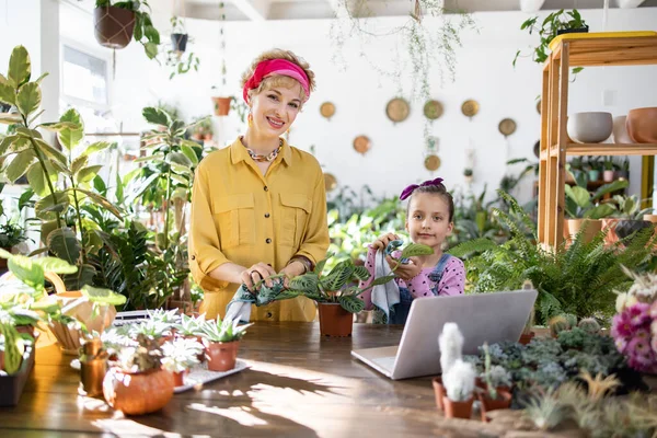 Bir kadın ve bir kız parlak, güneşli bir odada bitkilerle ilgileniyorlar, sıcak ve davetkar bir ortam yaratıyorlar.