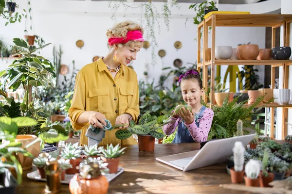 Bir anne ve kız, bitkileriyle parlak ve havadar bir serada ilgilenmekten zevk alır.