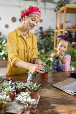 Bir kadın ve çocuk, parlak ve davetkar bir ev ortamında çiçeklerle ilgileniyorlar.