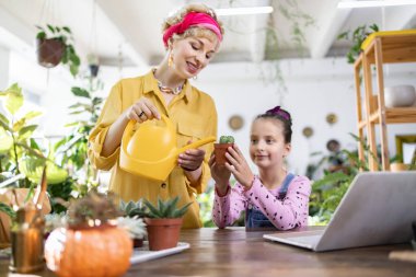 Bir kadın ve genç bir kız birlikte küçük bir kaktüsü suluyorlar, yürek ısıtan bir an yaratıyorlar.