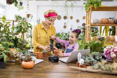 Bir kadın ve genç bir kız birlikte çiçek yetiştiriyorlar, aile ve doğa için iç açıcı bir manzara yaratıyorlar.