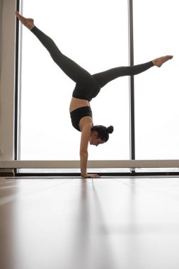 Atletizm dalında bir kadın, elleri ve bacakları ayrık bir şekilde ellerini dengede tutar. Kapalı alanda zorlu bir yoga duruşu sergiler.