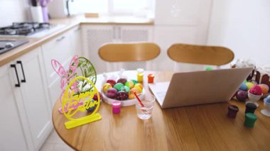 Paskalya yumurtası için bir mutfak masası renkli yumurtalar, boyalar ve ilham almak için bir dizüstü bilgisayar ile dekore edilir.