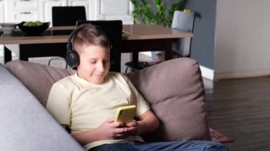 Kulaklıklı çocuk kanepede uzanmış akıllı telefon kullanıyor. İnternette geziniyor, oyun oynuyor ya da ders çalışıyor. Ev içi arkaplan