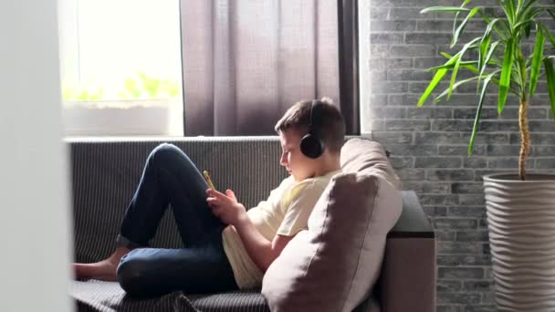 Niño Auriculares Tumbado Sofá Usando Teléfono Inteligente Desplazándose Través Internet — Vídeo de stock