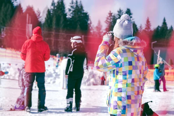 Estación de esquí, una chica mira a la montaña de esquí en la que los esquiadores están bajando —  Fotos de Stock