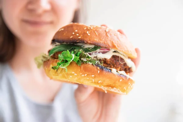 Vegan burger closeup in girl hands. Happy woman tasting and biting burger