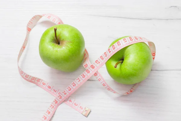 Maßband um zwei grüne Äpfel auf weißem Hintergrund gewickelt, Konzept des Ziels, Gewicht zu verlieren, das Ziel der Ernährung — Stockfoto