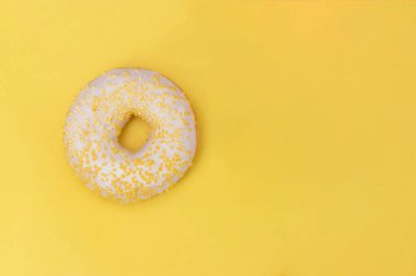 Beyaz şekerli donut ve sarı hamur kırıntıları serpiştirilmiş, üzerinde kopya alanı olan sarı bir arkaplan.