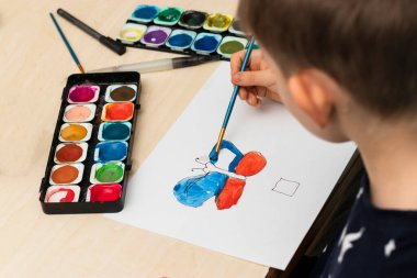 Ev ödevi yapan sevimli çocuk, boyama sayfaları, yazı ve resim. Çocuklar resim yapar. Yaratıcı çocuk. Eller boyalı, üst manzara,