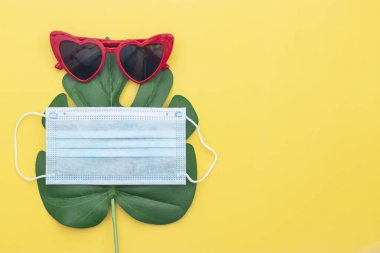 Kırmızı güneş gözlüğü, yeşil eğrelti otu yaprağı ve maske masa sarısında.,