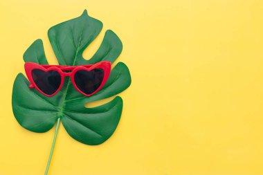 Kırmızı güneş gözlüğü, yeşil eğrelti otu yaprağı ve maske masa sarısında.,